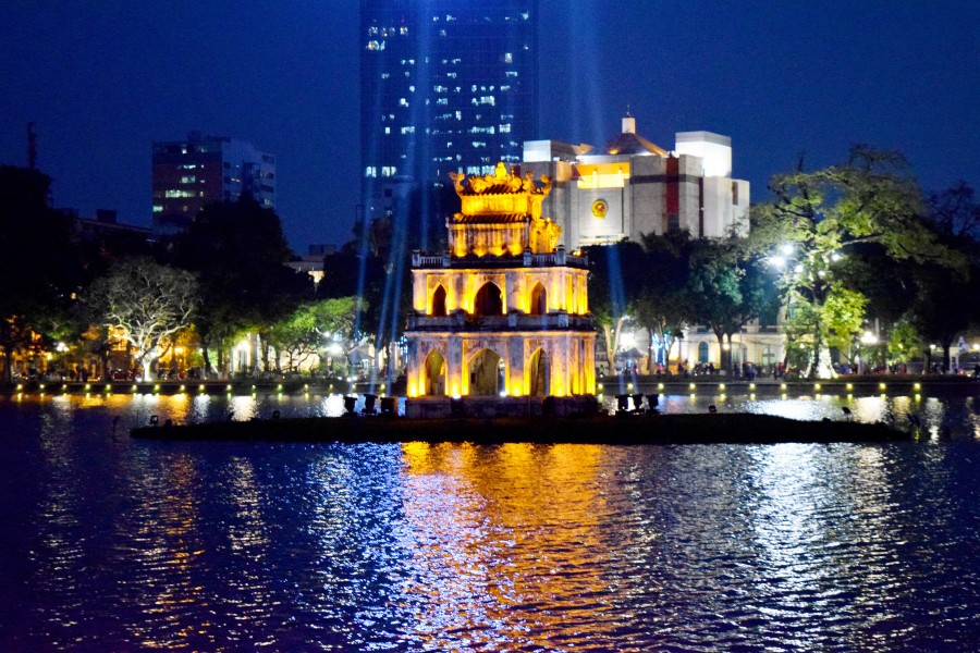 Une vue nocturne d'une pagode brillamment éclairée avec un toit doré, située sur le lac Hoan Kiem dans le vieux quartier de Hanoi.